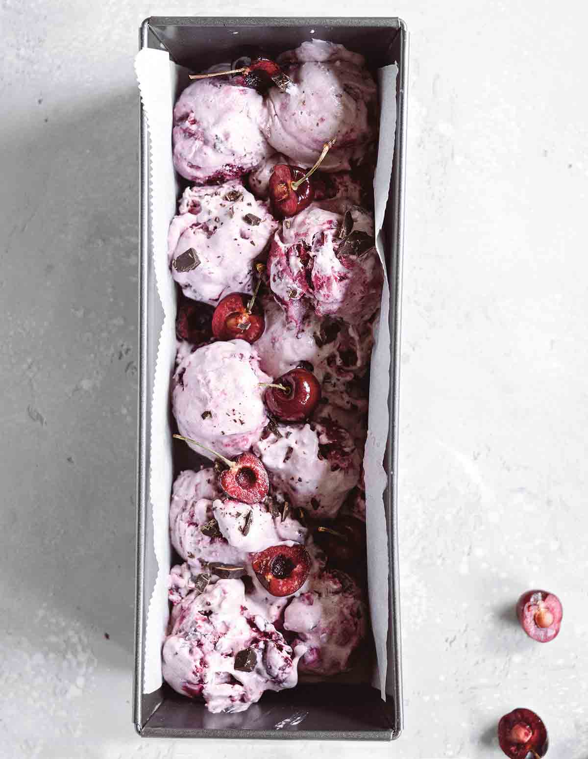 A parchment-lined metal tin filled with vegan chocolate cherry chunk ice cream and whole cherries on top.
