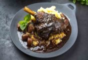 A grey plate topped with braised lamb, mashed potatoes, carrots, and gravy as an illustration of what is braising.