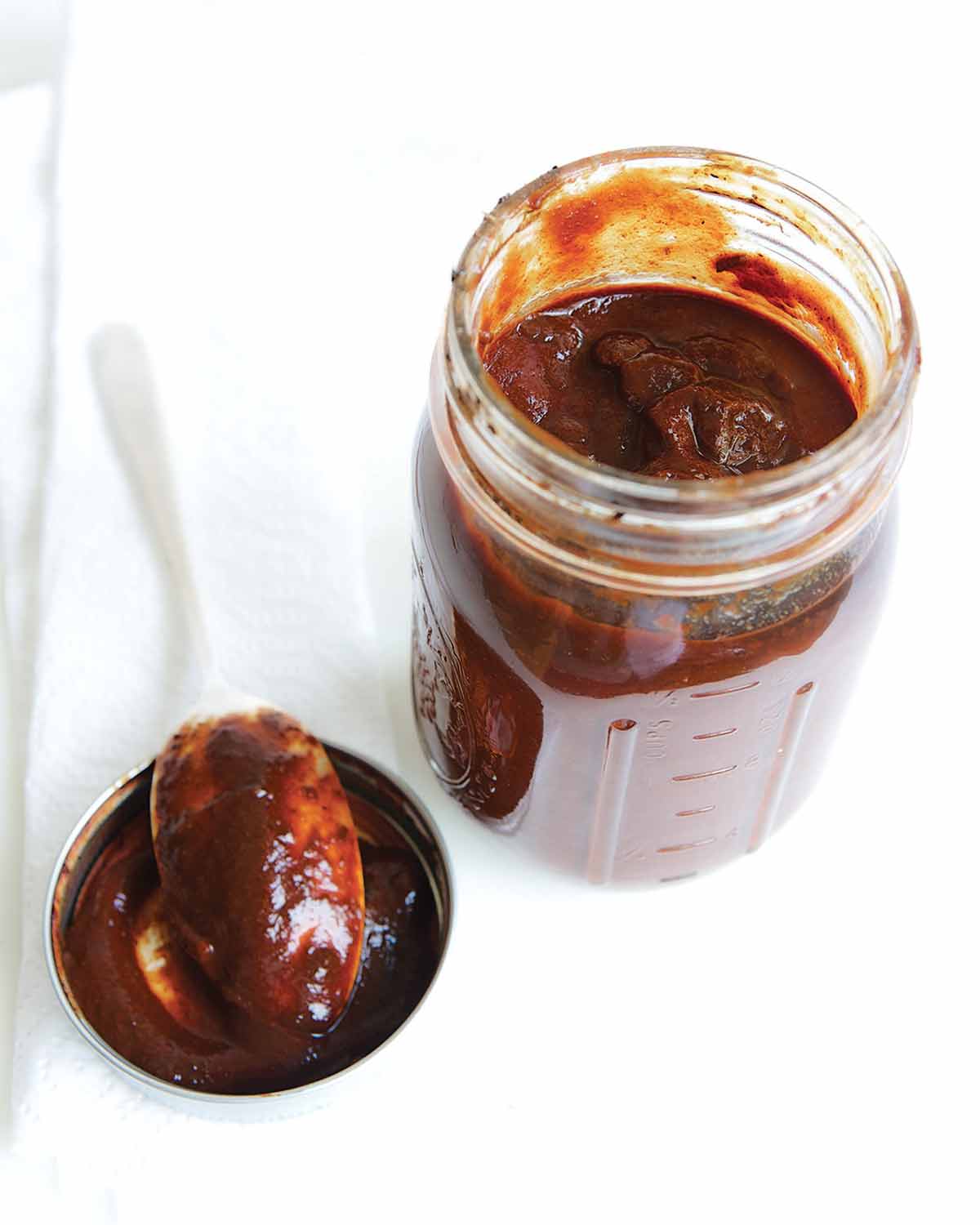 An open Mason jar of adobo sauce with a spoon resting on the lid beside it.