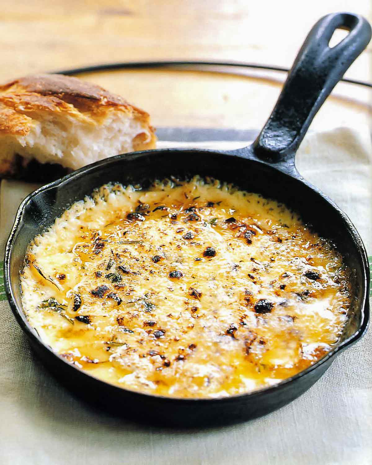 A cast iron skillet filled with bubbling baked fontina with garlic and thyme and a hunk of bread in the background.