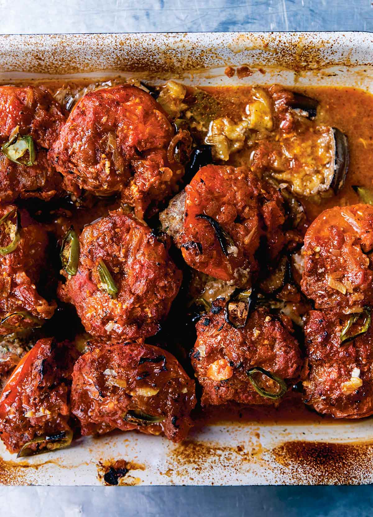 A ceramic baking dish filled with baked kofta -- meatballs on top of eggplant slices, all covered in tomato sauce.