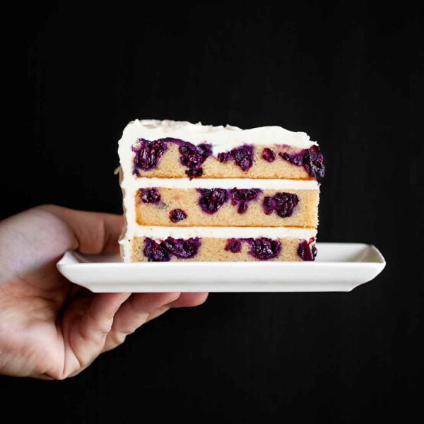 A white plate with a slice of blueberry-lemon layer cake