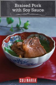 A patterned bowl with slices of braised pork with soy sauce on a red tray.