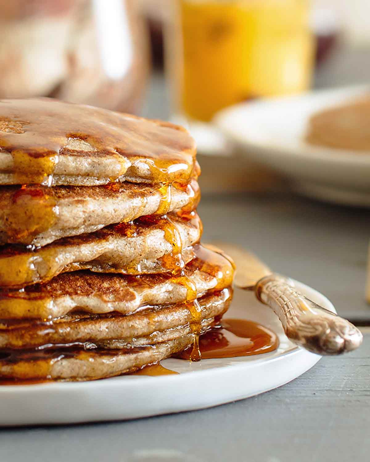 A stack of buckwheat pancakes on a white plate with maple syrup drizzled over them.