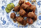 Skewers of bulgogi meatballs on a blue and white plate with pickles on the side.