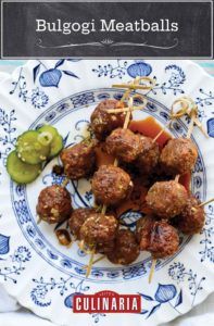 Skewers of bulgogi meatballs on a blue and white plate with pickles on the side.