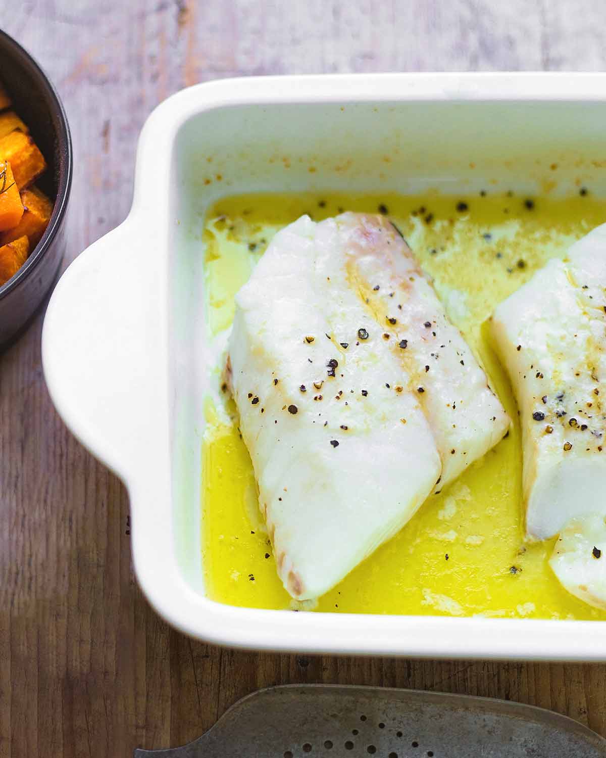 A white baking dish with pieces of butter baked fish seasoned with salt and pepper.