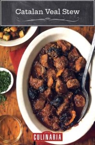 An oval dish of Catalan veal stew with prunes and potatoes on a wooden table with a dish of parsley next to it.