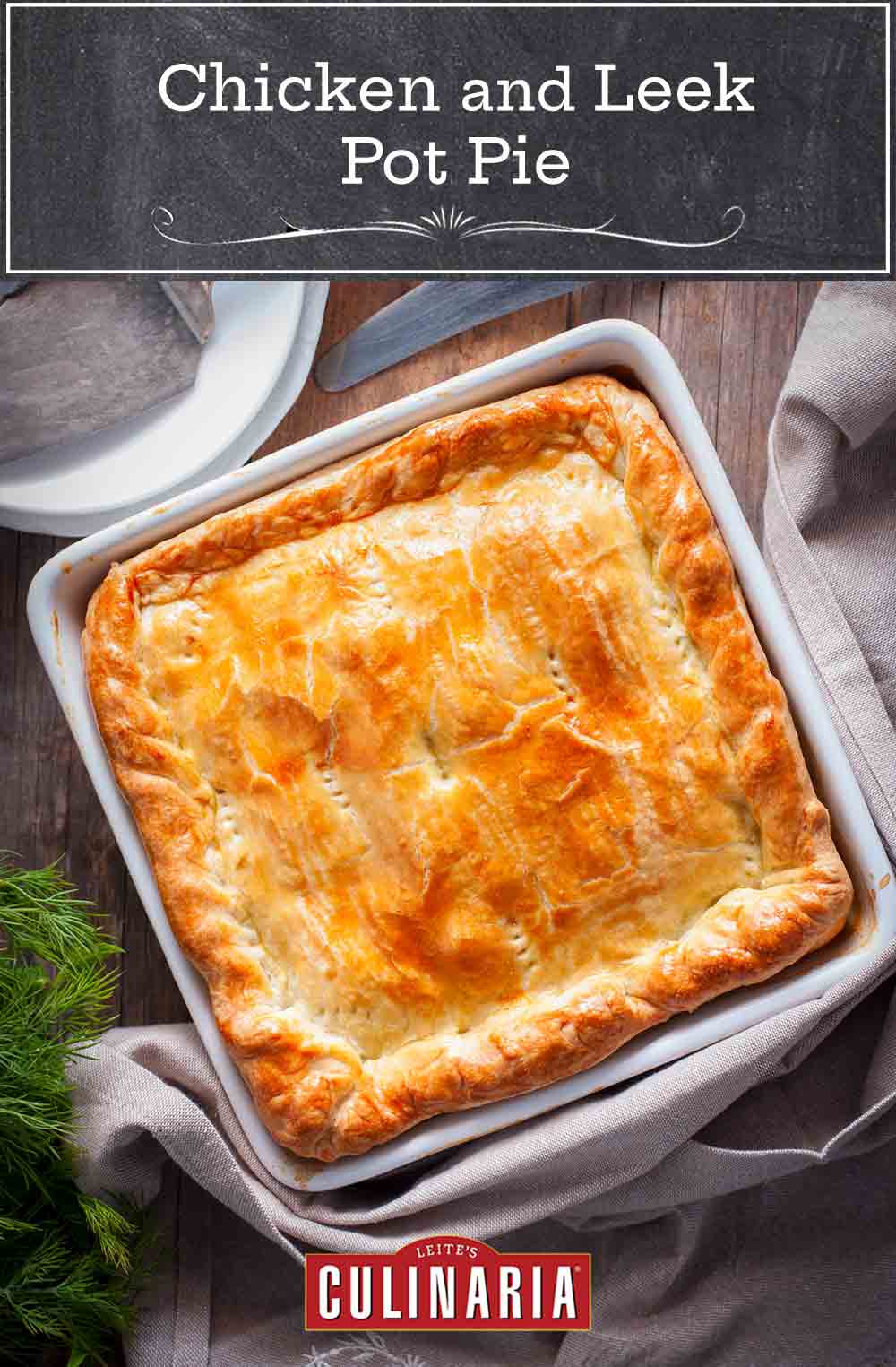 A chicken and leek pot pie in a white square baking dish with a server and forks and knife nearby.