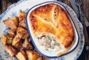 A chicken mushroom pot pie in a blue and white rectangular pie dish on a floral plate with fried potato chunks next to it.