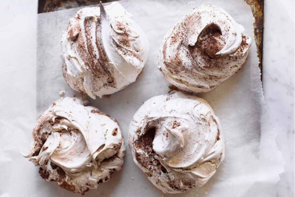 Four chocolate and cinnamon swirl meringues on a piece of parchment on a rimmed baking sheet.
