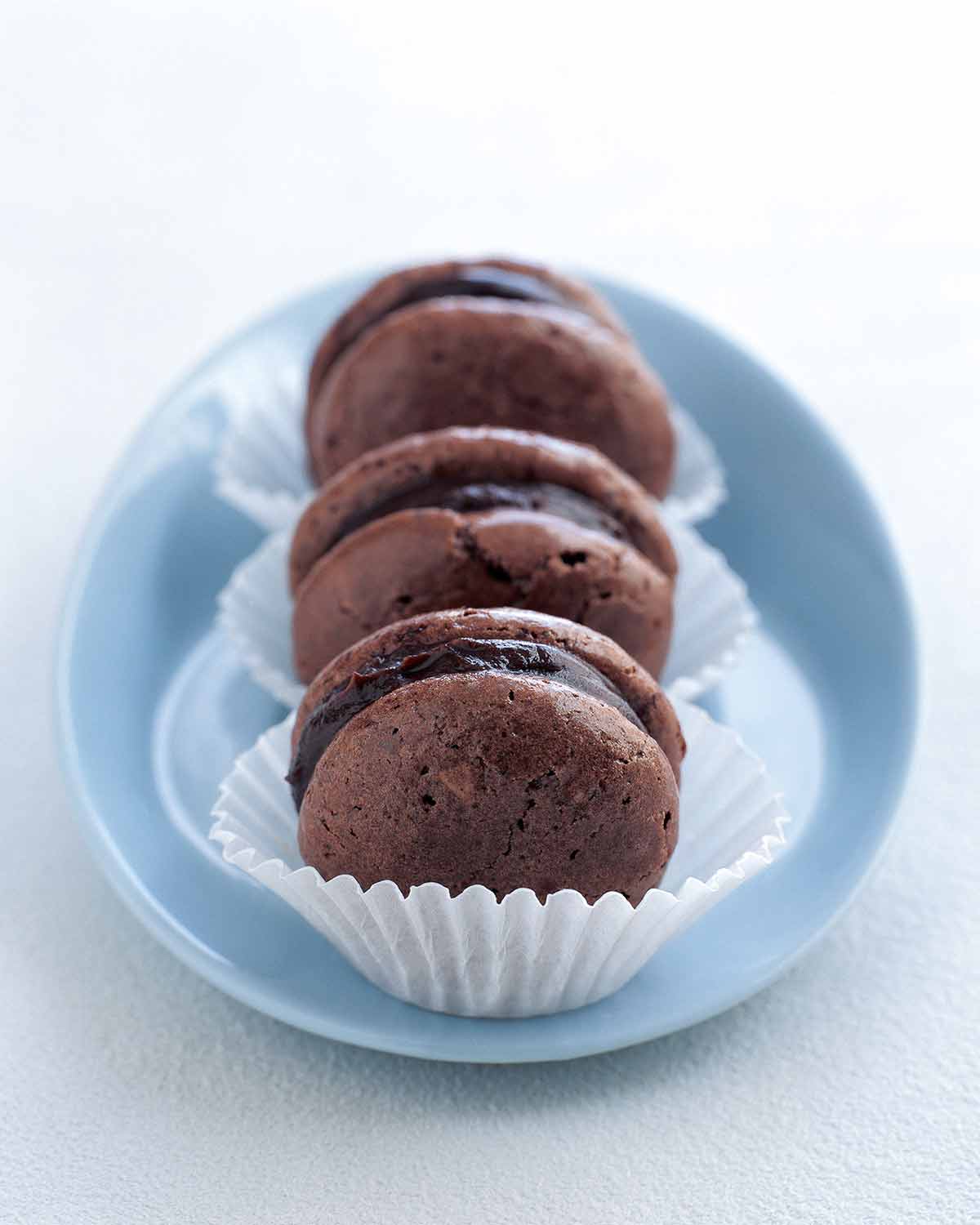 Three chocolate macarons in paper wrappers in a blue dish.