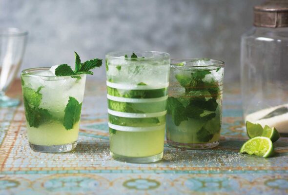 Three glasses of classic mojito, with two lime wedges and a jar of sugar beside them.