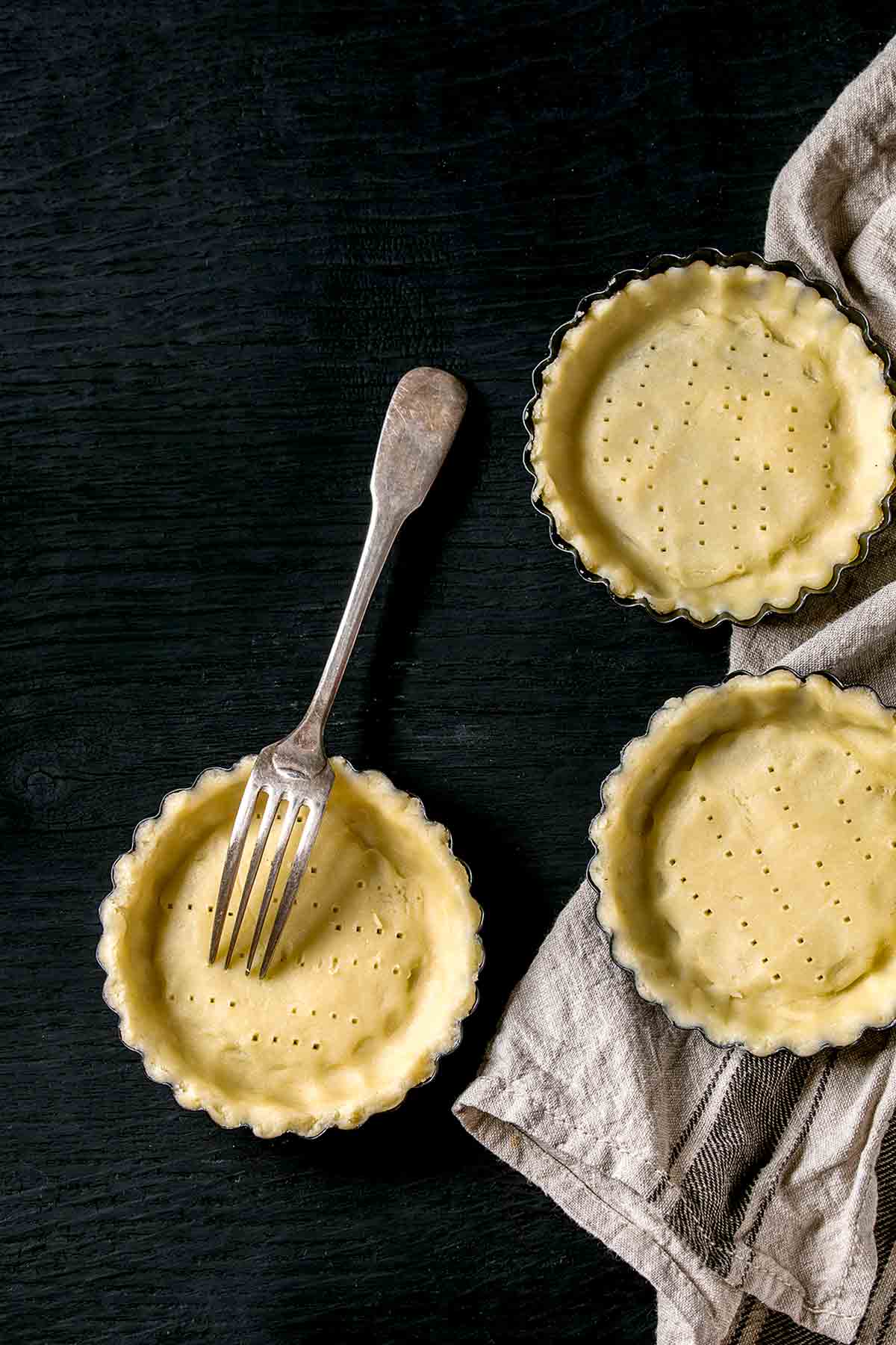 Three small pie shells that have been pricked with a fork with a fork resting in one of them.