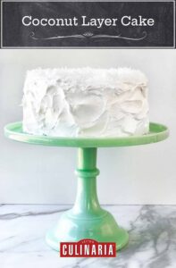 A white coconut layer cake, with 7-minute frosting topped with shredded coconut on a green cake stand