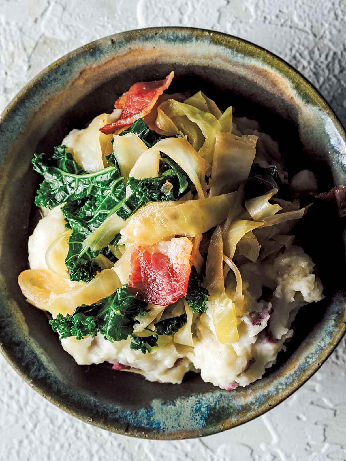 A ceramic bowl filled with Colcannon - an Irish dish made with mashed potatoes, cabbage, kale and bacon.