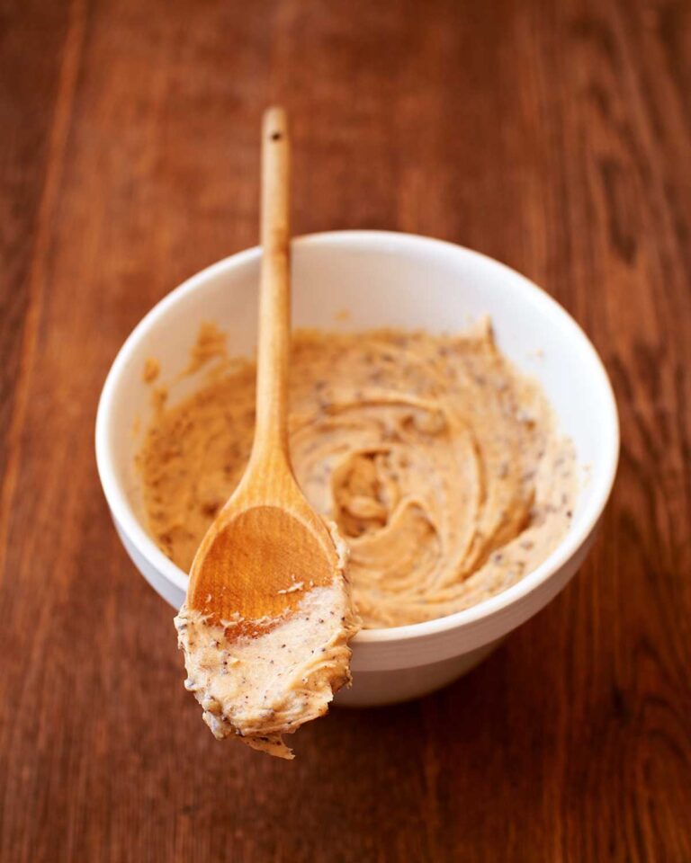 A white bowl partially filled with cookie dough buttercream frosting with a wooden spoon resting on top.