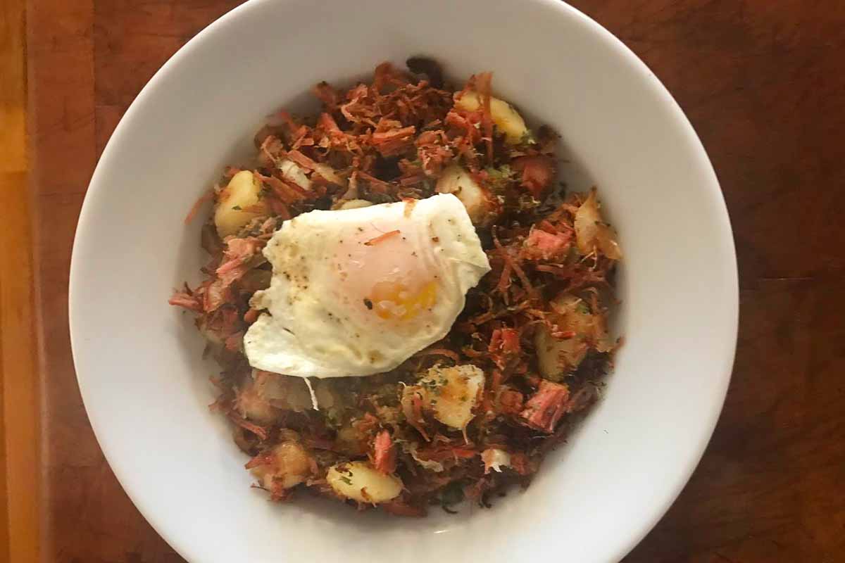 A white bowl filled with crispy homemade corned beef hash and topped with a perfectly fried egg.