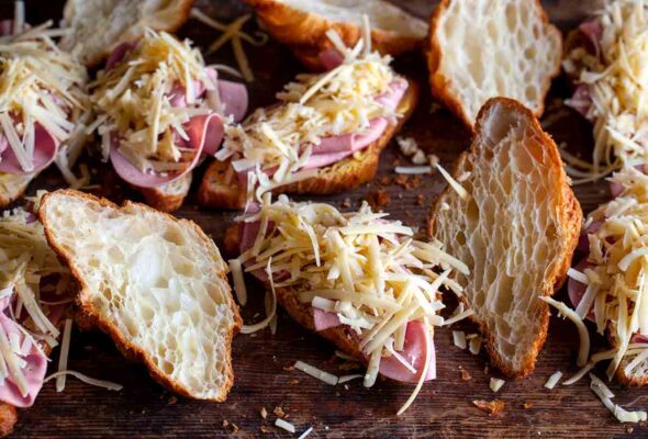 Halved croissants topped with ham and shredded cheese for a croque monsieur casserole.