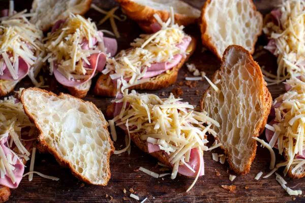 Halved croissants topped with ham and shredded cheese for a croque monsieur casserole.