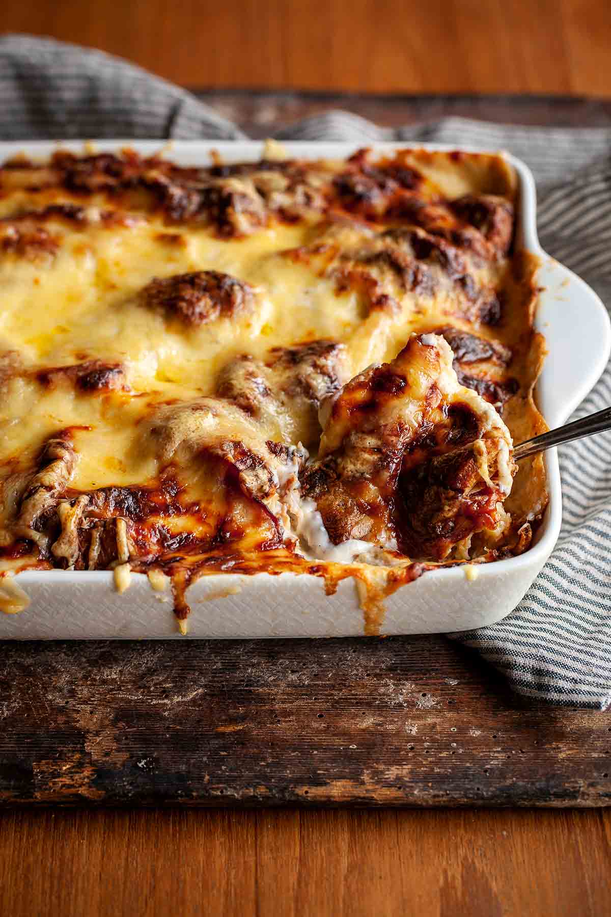 A cooked croque monsieur casserole in a white rectangular baking dish on a wooden board.