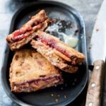 Three halves of deep-fried peanut butter and jelly sandwiches on a black oval platter with a knife on the side.