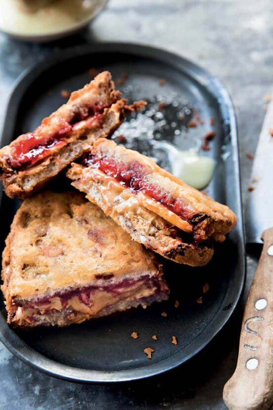 Three halves of deep-fried peanut butter and jelly sandwiches on a black oval platter with a knife on the side.