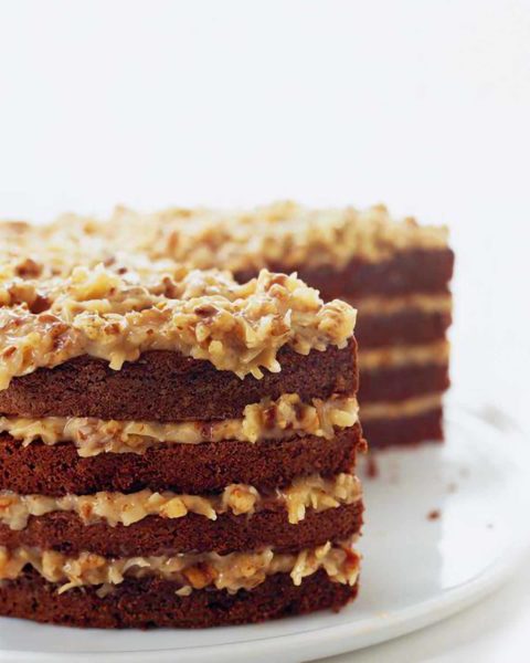 A layered German chocolate cake with coconut pecan frosting on a platter with a few slices cut from it.