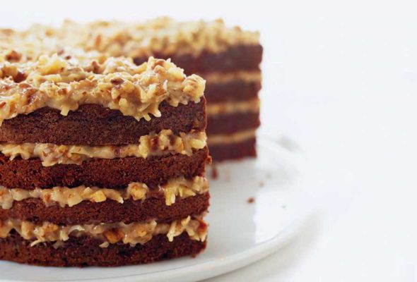 A layered German chocolate cake with coconut pecan frosting on a platter with a few slices cut from it.