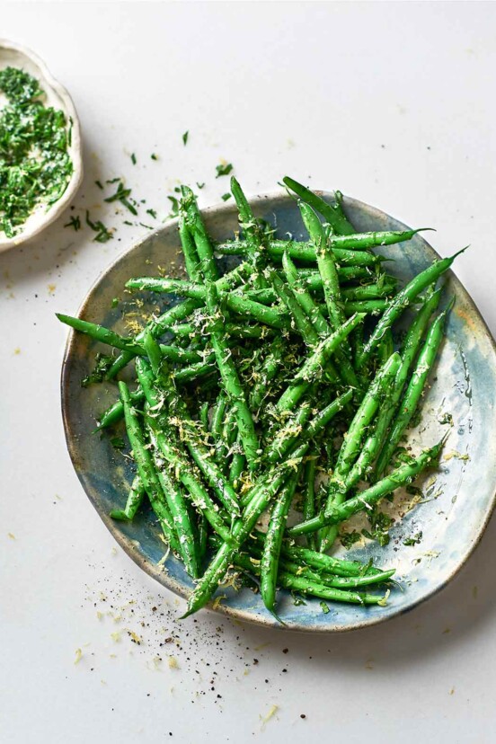 A bowls of green beans gremolata with a small dish of gremolata on the side.