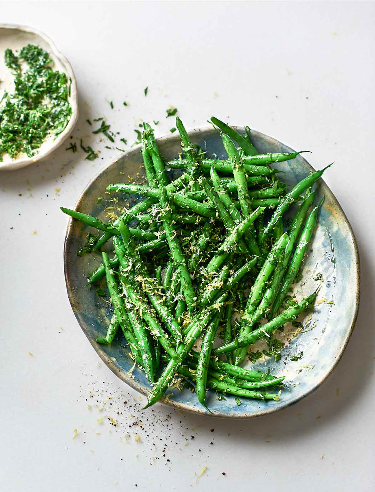 A bowls of green beans gremolata with a small dish of gremolata on the side.