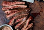 A sliced grilled flank steak with a bowl of seasoning mix and a knife on the side.