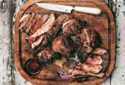 A carved grilled leg of lamb on a wooden cutting board with a knife resting beside it.