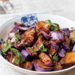 A white bowl filled with Hakka eggplant, garnished with fresh basil.