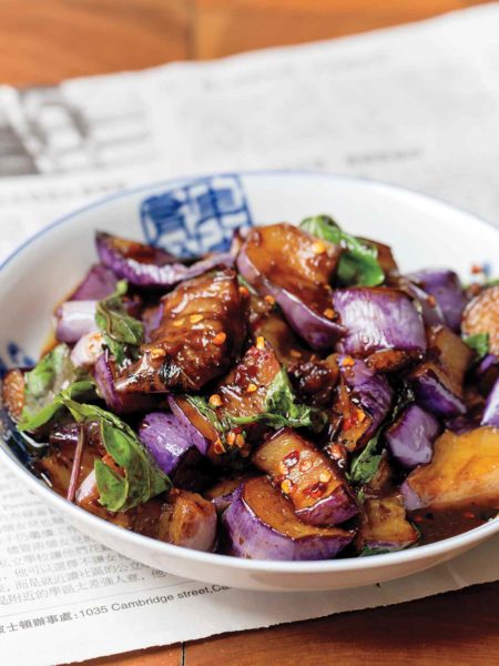 A white bowl filled with Hakka eggplant, garnished with fresh basil.