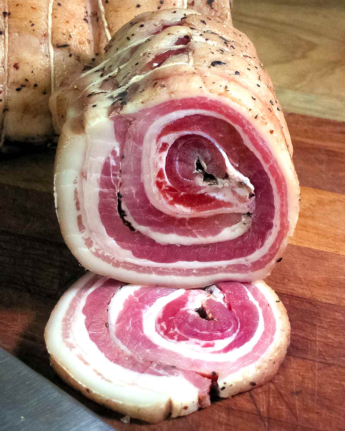 A piece of homemade pancetta sliced to show the circular pattern.