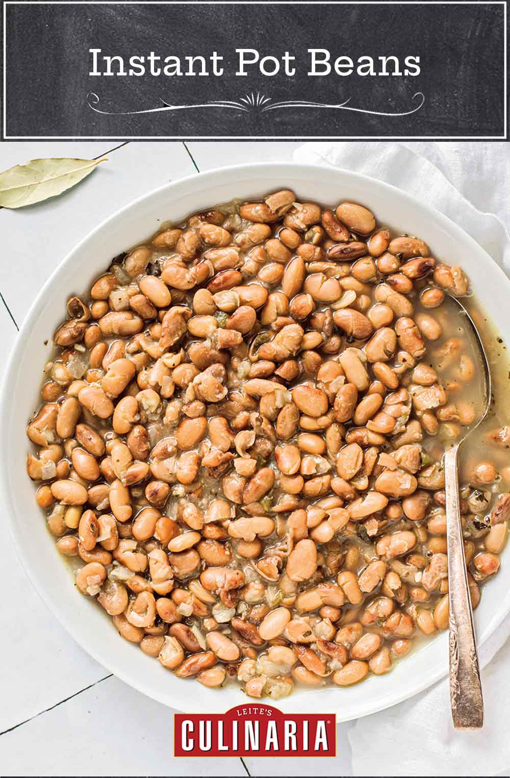 A large white bowl filled with Instant Pot beans, with a spoon resting inside and a bay leaf nearby.