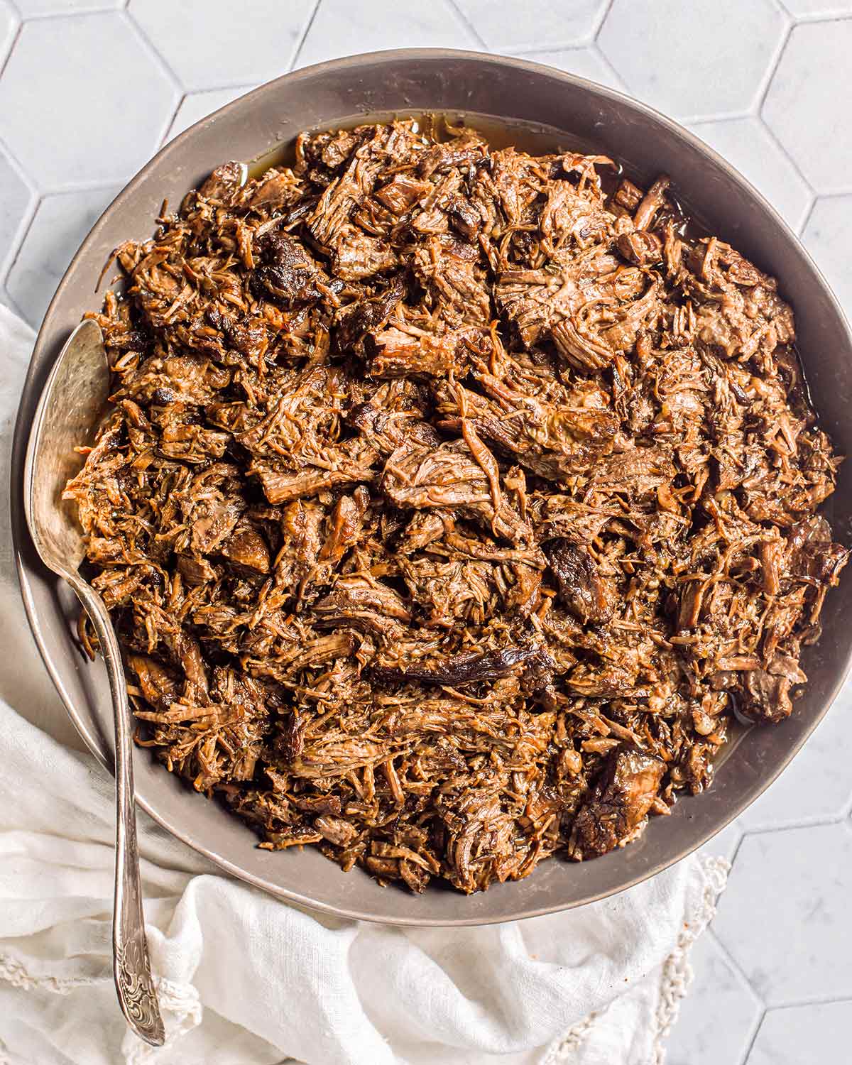 A bowl of shredded beef from an Instant Pot chuck roast with a silver spoon resting in the bowl.