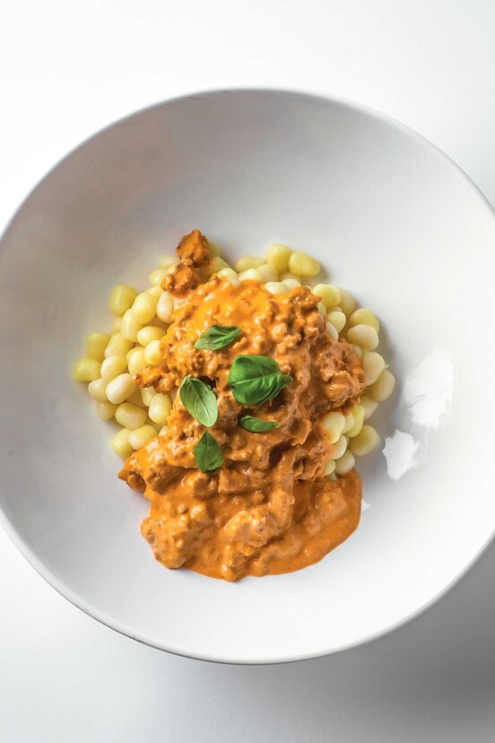 A white bowl filled with leftover meatloaf gnocchi in a creamy tomato sauce that's garnished with fresh basil.
