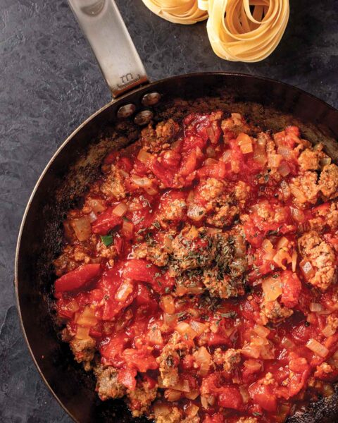 A skillet filled with leftover meatloaf pasta sauce, with a pile of pasta on the side.