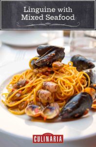 A white bowl filled with linguine with mixed seafood, including mussels and clams.