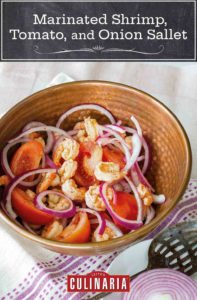 A brown bowl filled with marinated shrimp, tomato, and onion sallet, on a white and purple towel with a slotted spoon and half of a red onion resting on a plate beside the salad.