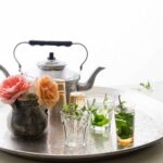 A teapot, a collection of glasses, three partially filled with mint tea, and a vase of flowers on a silver tray.