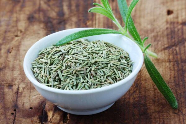 A bowl of dried rosemary leaves with a sprig of fresh rosemary beside it in response to the question 'how do I substitute dried herbs for fresh?'