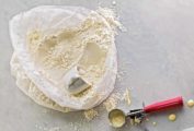 A plastic bag filled with homemade pancake mix and cup resting in the mix and a wet ice cream scoop on the side.