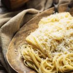 A wooden bowl filled with pasta with butter and Parmesan on a brown linen cloth.