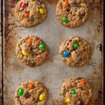 Six peanut butter-oatmeal-chocolate chip cookies on a rimmed baking sheet.