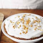 A whole peanut butter pie in a white pie dish, topped with whipped cream and peanuts.