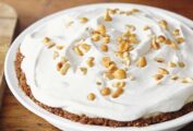 A whole peanut butter pie in a white pie dish, topped with whipped cream and peanuts.