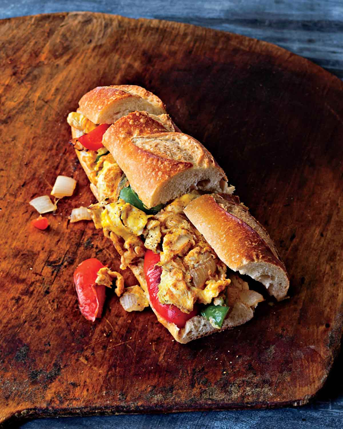 A pepper and egg sandwich on a wooden table with pieces of pepper and onion falling out.